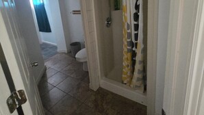 Un baño con ducha, inodoro y una puerta que da a otra habitación.