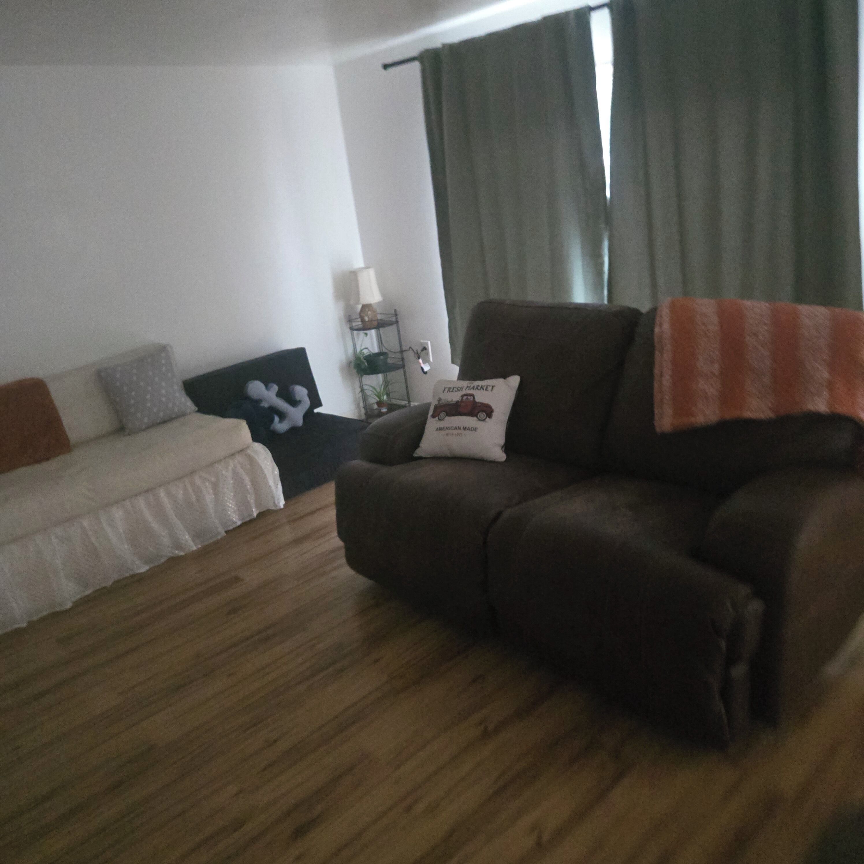 A room with a bed, a sofa, a small table with a lamp, and a window with curtains.