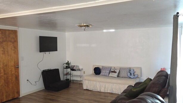 Una sala de estar con un sofá, un sillón negro, un televisor montado en la pared y un ventilador de techo.