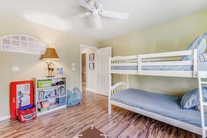 A bunk bed room with a ceiling fan, a bookshelf, and a door leading to another room.