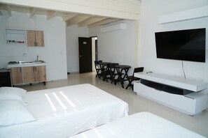 A hotel room with a bed, a TV, a desk, and a kitchenette.