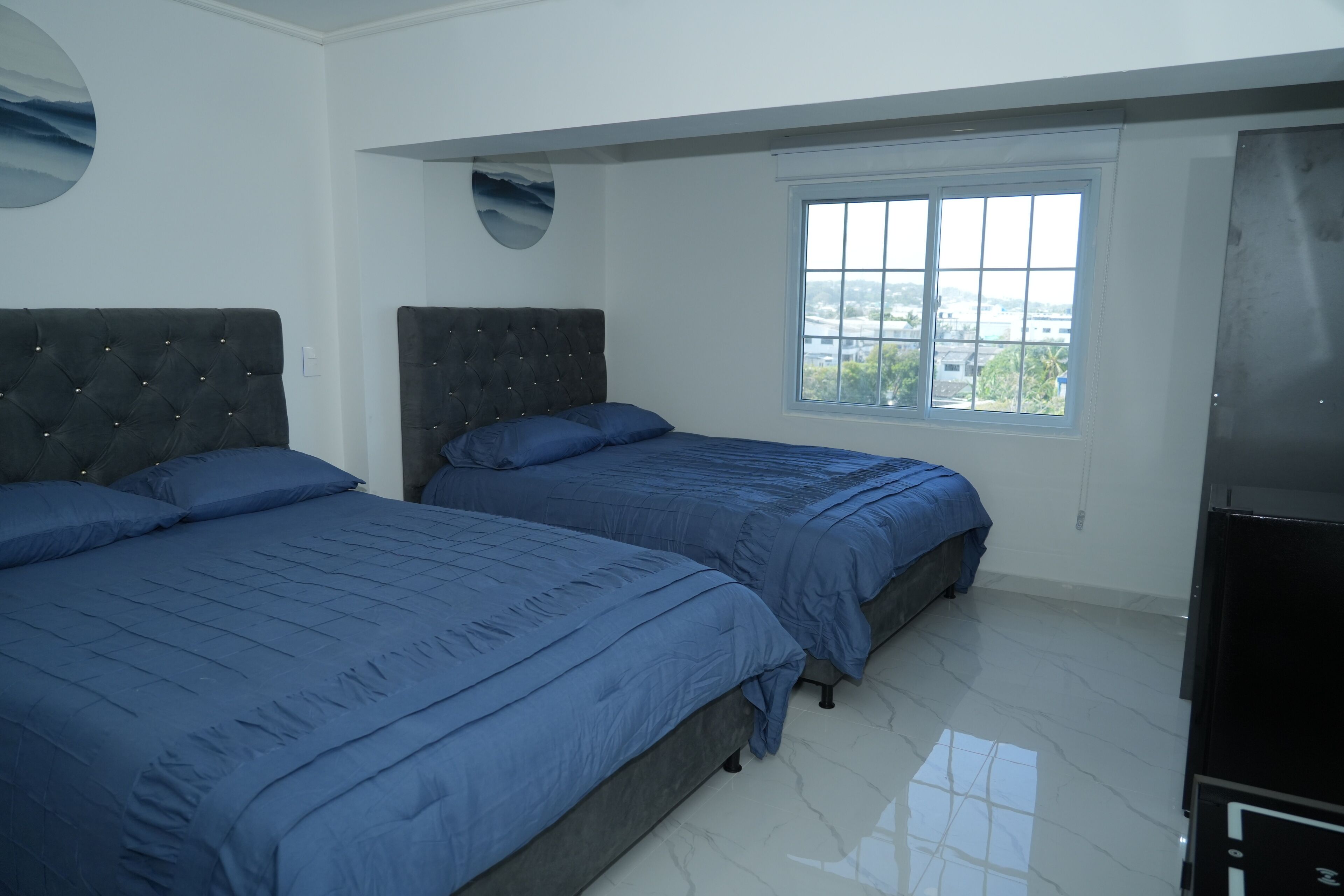 Un dormitorio con dos camas, una ventana y una lámpara fijada a la pared.