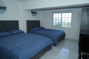 A bedroom with two beds, a window, and a wall-mounted light fixture. - Jhonny Cay Suites (San Andrés)