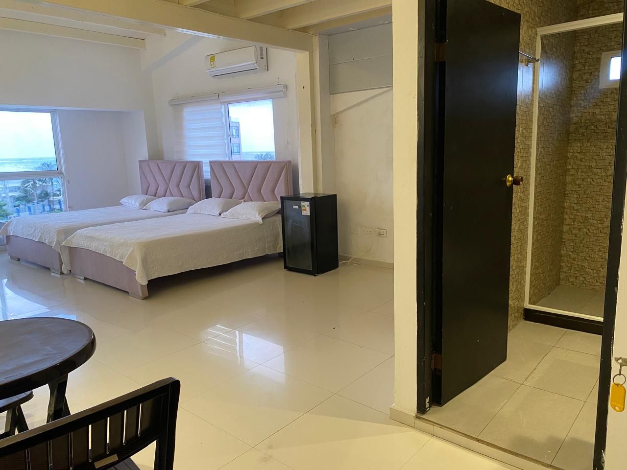 Una habitación con dos camas, una mesita y una puerta que da a un baño.