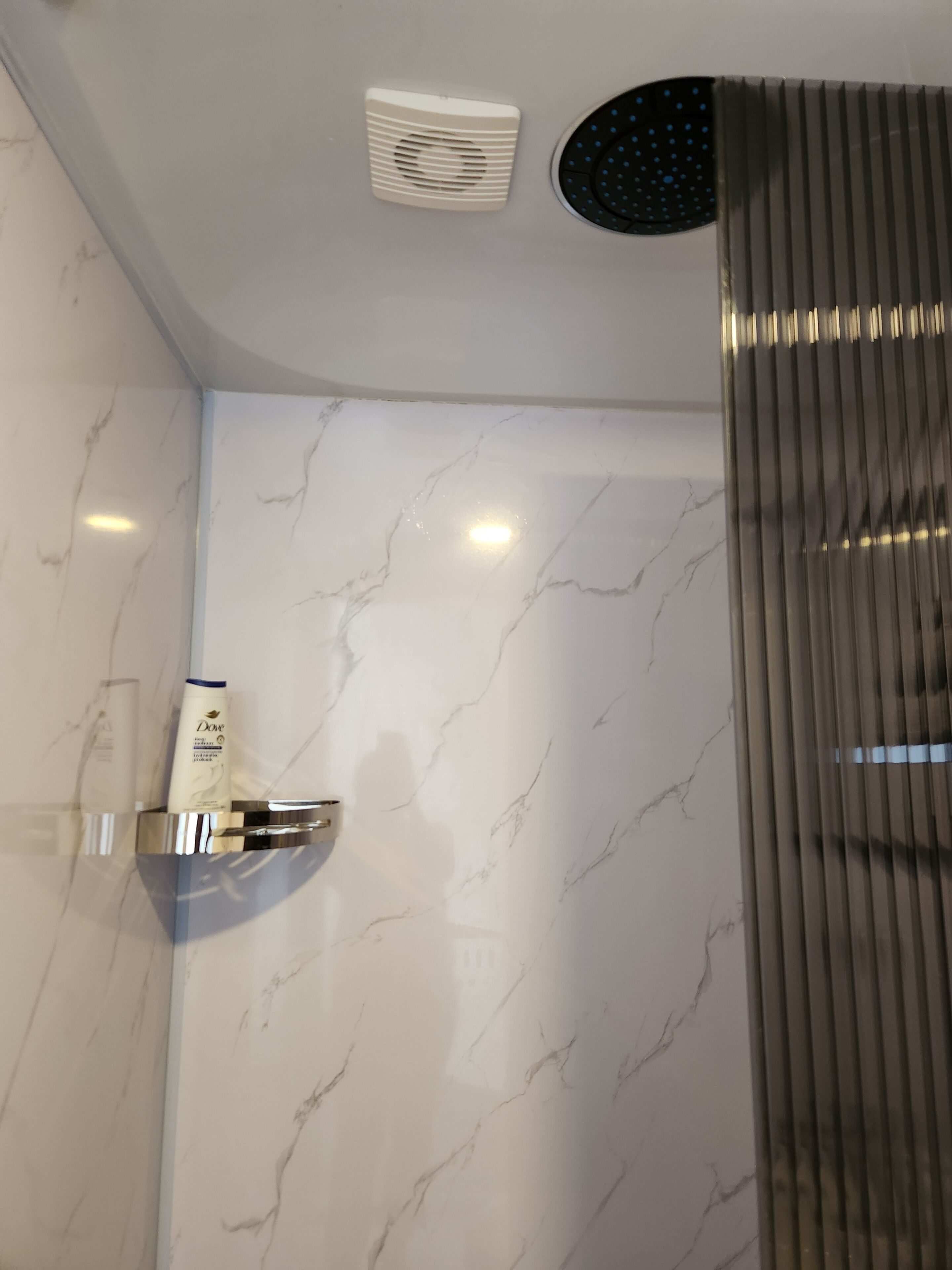 Un baño con pared de mármol, ducha con puerta de vidrio curva y un secador de manos montado en la pared.