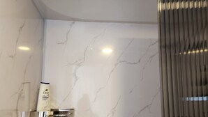 A bathroom with a marble wall, a shower with a curved glass door, and a hand dryer mounted on the wall. - Luxury Riverside Dome with Private Bathroom Near Bragg Creek (Calgary)