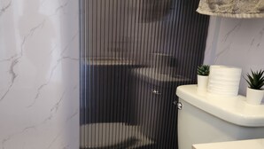 Kylpyhuone, jossa on wc, suihkukaappi, marmoriseinä ja pyyheteline.