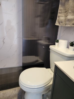 A bathroom with a toilet, a shower enclosure, a marble wall, and a towel rack.