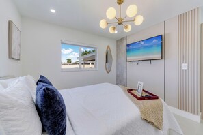 Ein Schlafzimmer mit Bett, Fenster, Fernseher und Deckenleuchte.