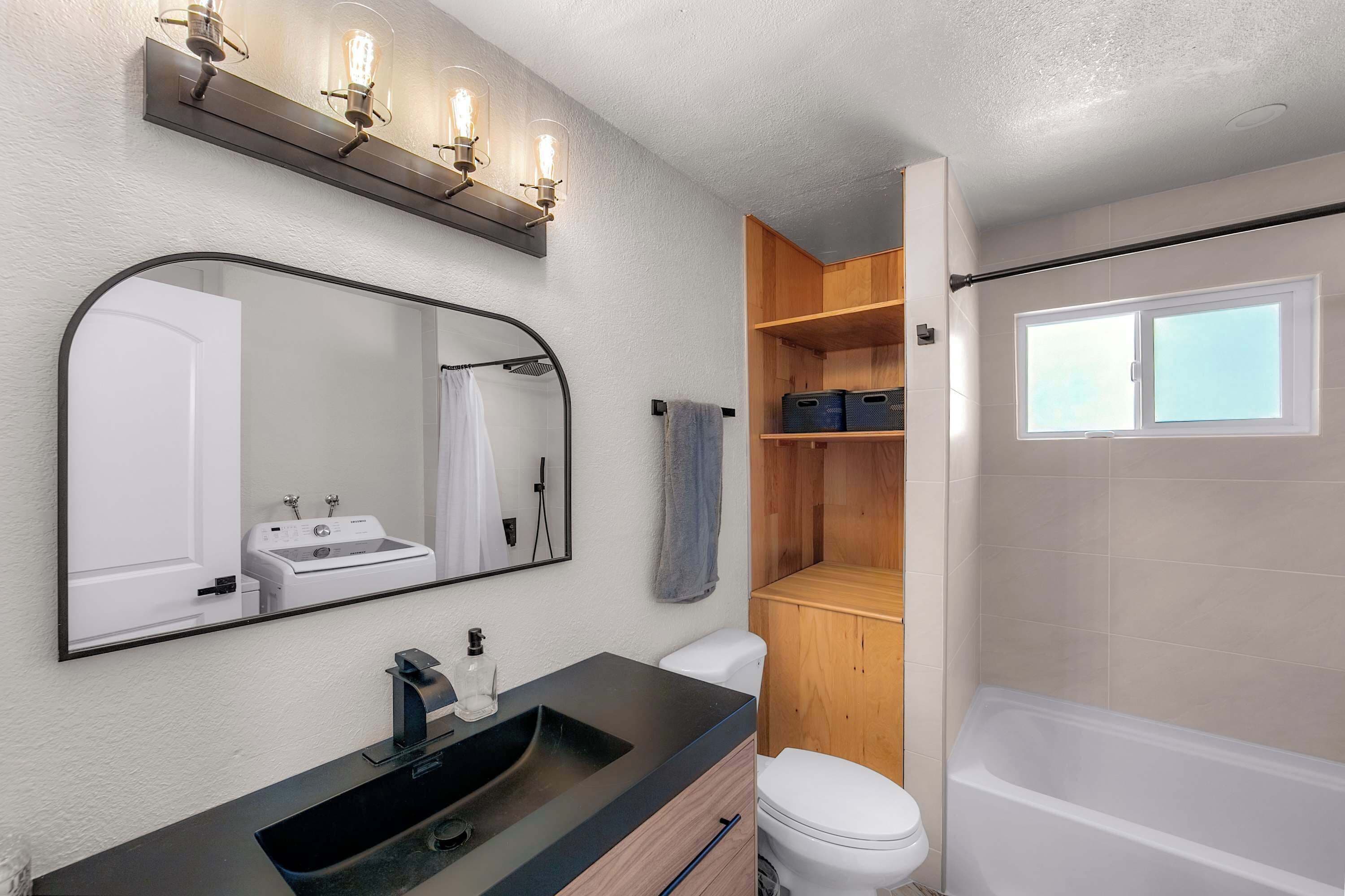 Un baño moderno con un espejo grande, un lavamanos, un inodoro y una zona de ducha.