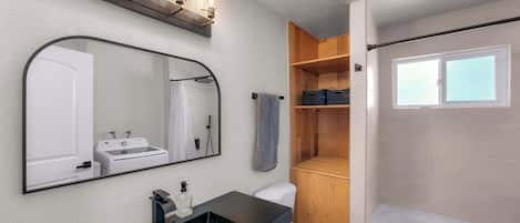 Un baño moderno con un espejo grande, un lavamanos, un inodoro y una zona de ducha.