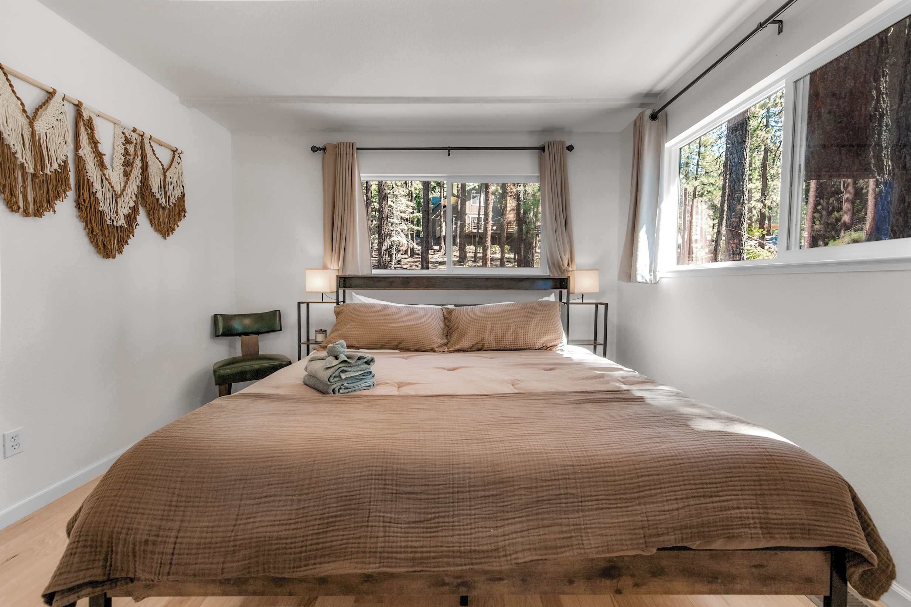 Une chambre avec un grand lit, une fenêtre donnant sur la forêt et une décoration murale en macramé.
