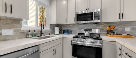 A modern kitchen with stainless steel appliances, white cabinetry, and a window with blinds.