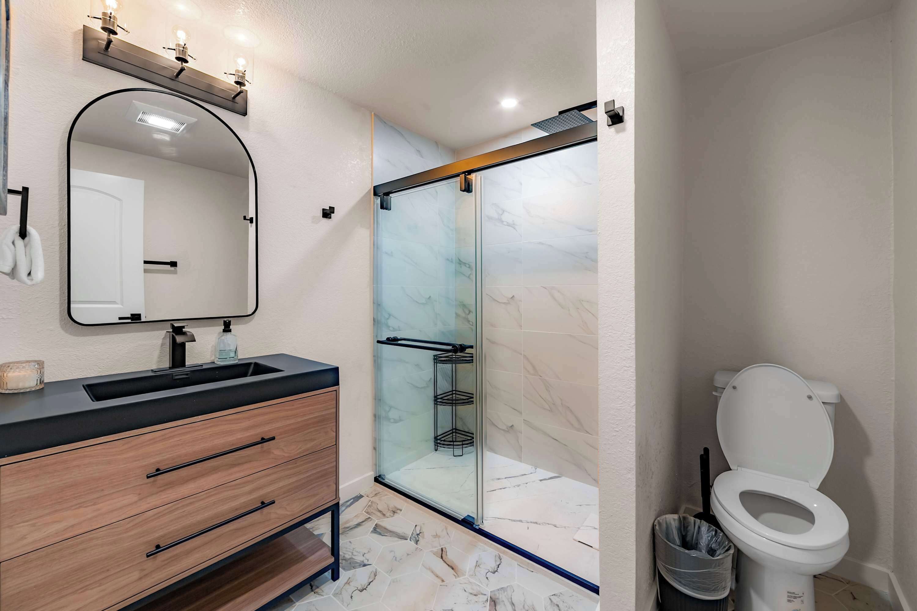 Et moderne badeværelse med en glasbrusekabine, et trækommode med spejl og et hvidt toilet.