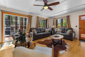 Ein geräumiges Wohnzimmer mit zwei Sofas, einem Couchtisch, einem Deckenventilator und großen Fenstern.
