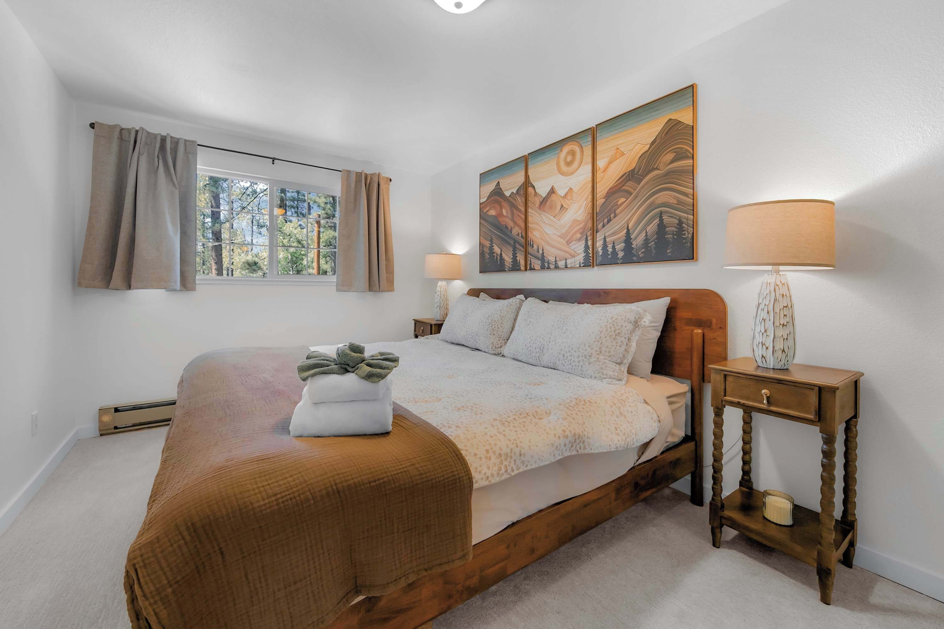 A bedroom with a large bed, a window with curtains, a painting above the bed, and a bedside table with a lamp.