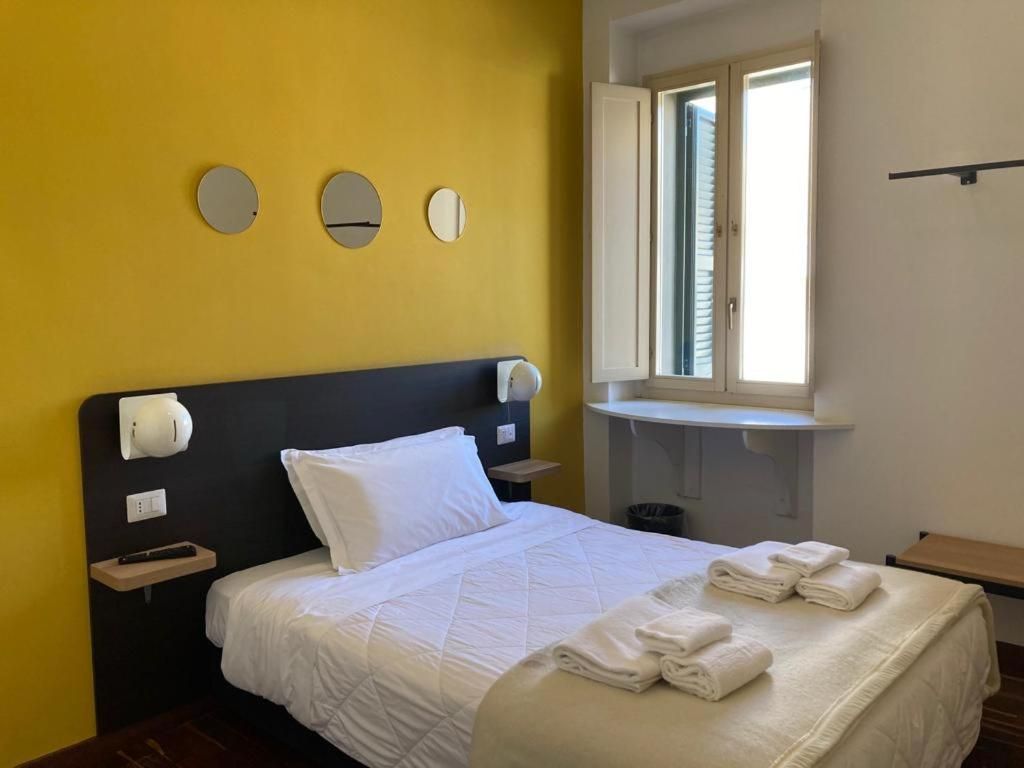 A hotel room with a bed, a bedside table, a nightstand, a window, and a wall-mounted mirror.