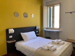 A hotel room with a bed, a bedside table, a nightstand, a window, and a wall-mounted mirror. - Il Piccoloalbergo (Matera)