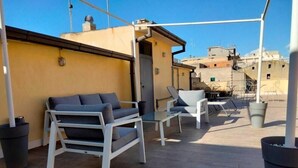 Een terras op het dak met buitenmeubels, waaronder een bank en stoelen, en een potplant.