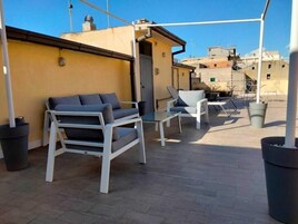 Una terrazza sul tetto con posti a sedere all'aperto, tra cui un divano e delle sedie, e una pianta in vaso.