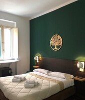 Una camera d'albergo con un letto, due lampade ai comodini, un decoro a forma di albero appeso al muro e una finestra con tende.