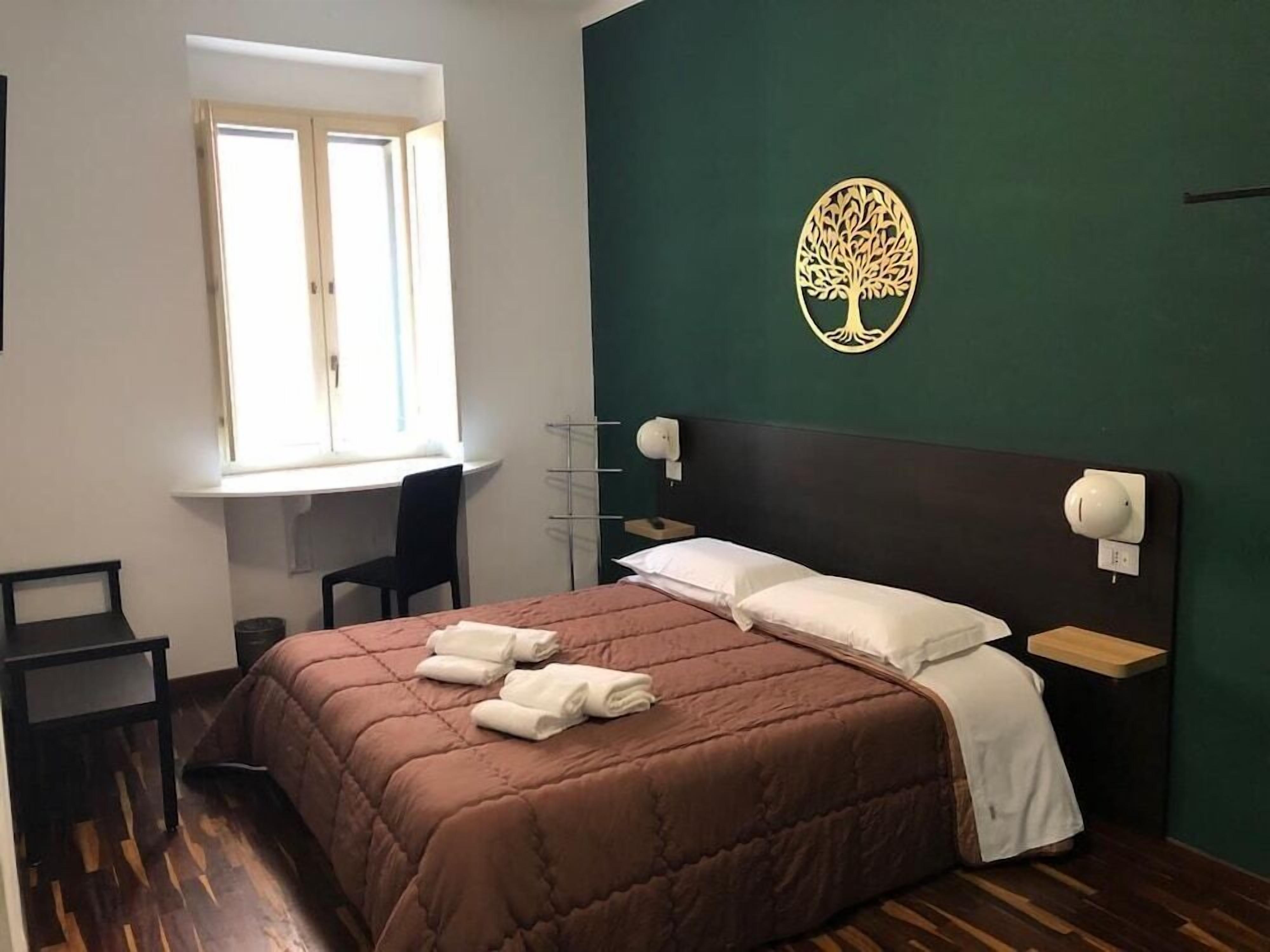 A bedroom with a bed, a desk, a chair, a window, and a wall-mounted tree decoration.