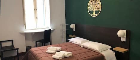 A bedroom with a bed, a desk, a chair, a window, and a wall-mounted tree decoration.