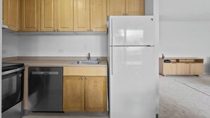 Una cocina con armarios de madera, un refrigerador de acero inoxidable, un lavavajillas y un lavamanos en la encimera.