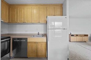 A kitchen with wooden cabinets, a stainless steel refrigerator, a dishwasher, and a countertop sink. - Cozy Island Escape - Near Waikiki & Diamond Head (Honolulu)
