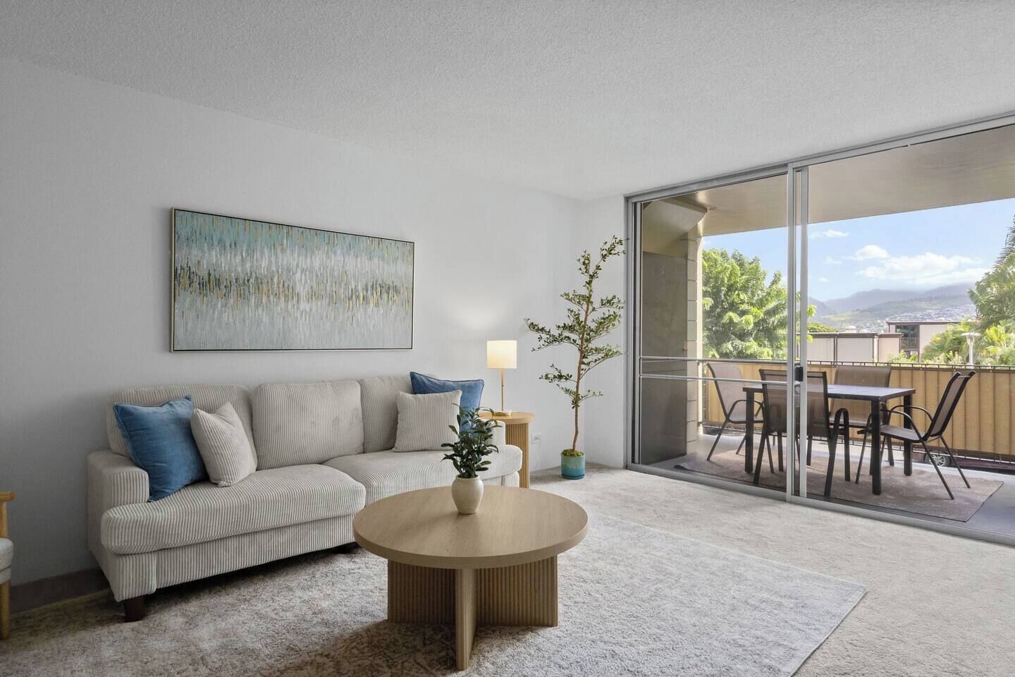A modern living room with a sofa, coffee table, and a view of the outdoors through a sliding glass door.