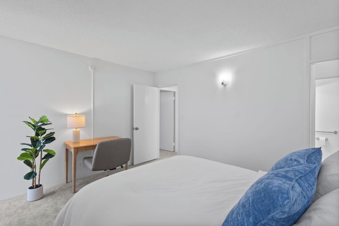 Ein Hotelzimmer mit einem Bett, einem Schreibtisch, einem Stuhl, einer Lampe und einer Zimmerpflanze.