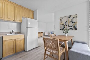 A modern kitchen with wooden cabinets, a white refrigerator, and a dining area with a table and chairs. - Cozy Island Escape - Near Waikiki & Diamond Head (Honolulu)