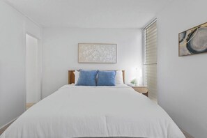 Une chambre à coucher avec un lit, une table de chevet, une lampe fixée au mur et un tableau encadré.