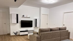 Een moderne woonkamer met een flatscreen televisie, een grijze bank, een salontafel en een witte dressoir.