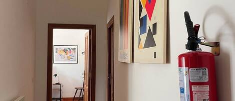 A hallway with wooden flooring, a fire extinguisher mounted on the wall, and framed artworks.