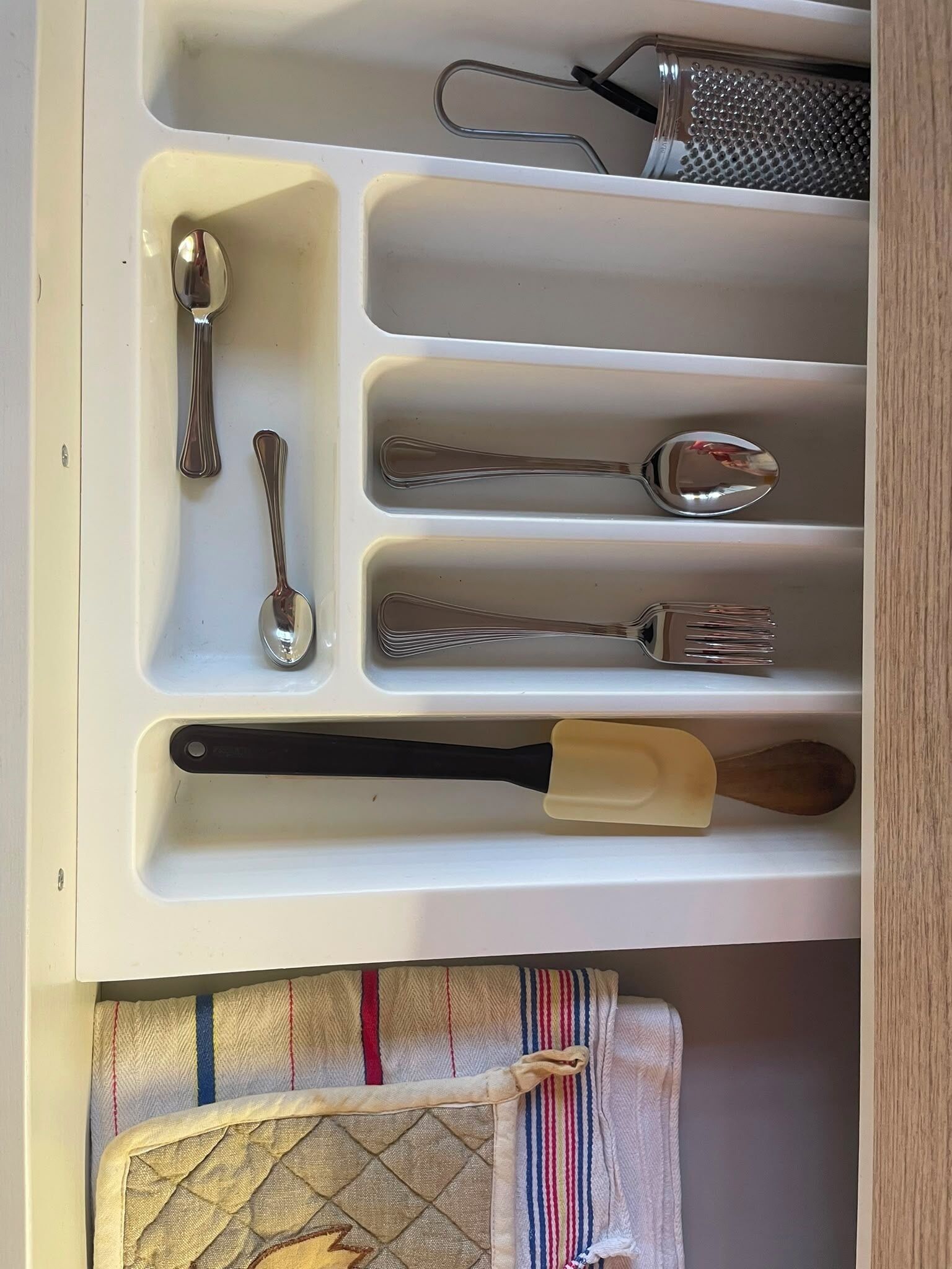 A drawer with compartments containing various kitchen utensils including spoons, a whisk, and a grater.