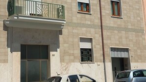 Ein mehrgeschossiges Gebäude mit flacher Fassade, Balkonen mit Metallgeländern und einem davor parkenden Auto.