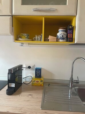 A kitchen with a yellow shelf above the counter, a coffee maker, a box of Lipton tea, and a sink.