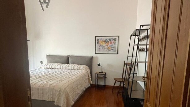 Ein Schlafzimmer mit einem Bett, einem Nachttisch, einem Stuhl, einer Leiter und einer Tür.