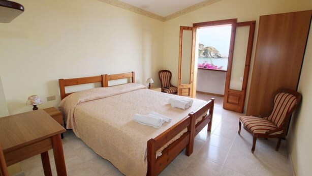 Un dormitorio con una cama doble, dos sillas, una mesita y un balcón con vistas.