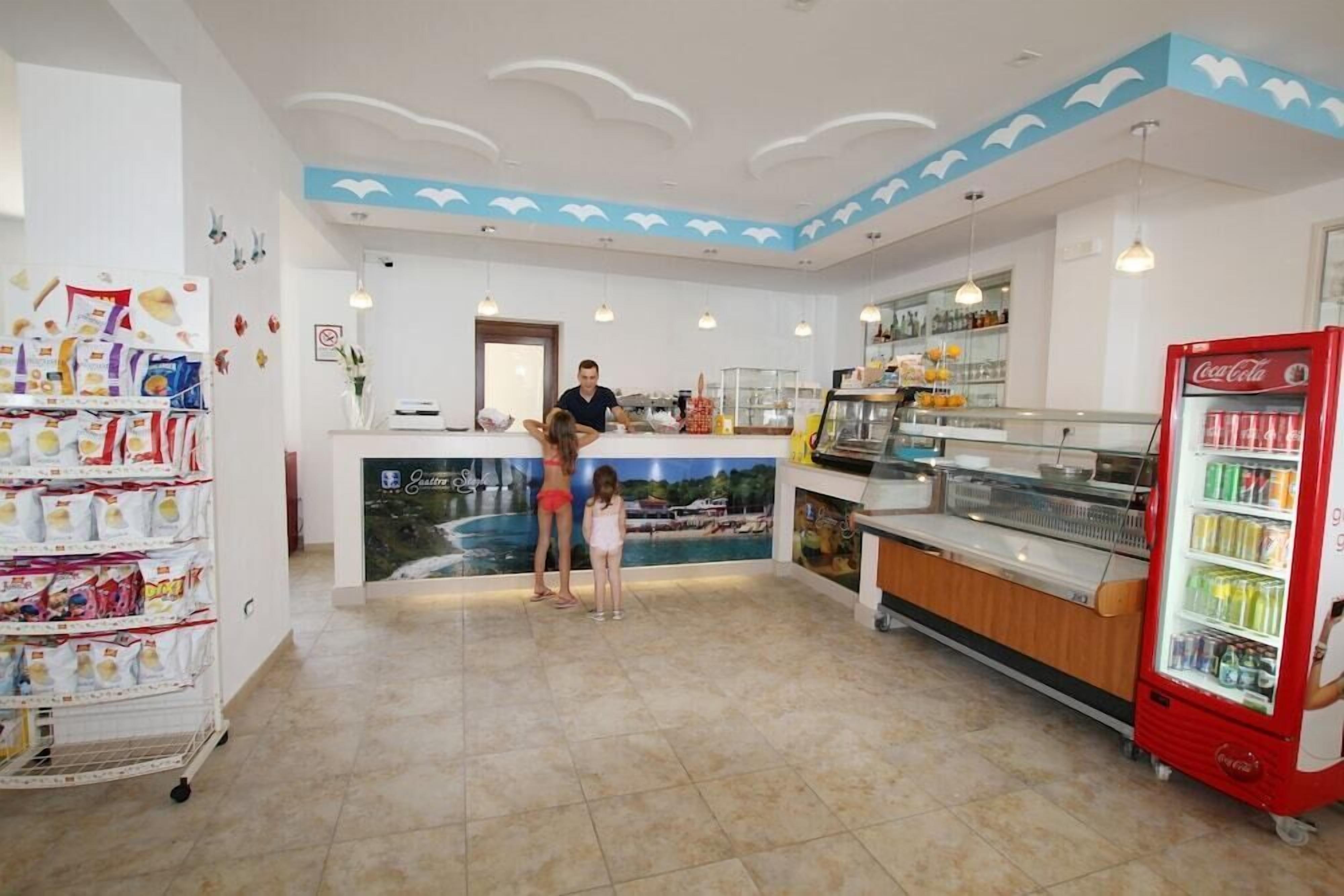 A restaurant with a counter, a Coca-Cola refrigerator, and a wall with a tropical mural.