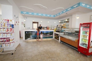 Un restaurante con mostrador, un refrigerador de Coca-Cola y una pared con un mural tropical.