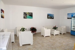 Un área de recepción con muebles de mimbre blancos, un mostrador de recepción y dos cuadros colgados en la pared.