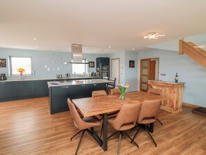 A modern kitchen with a central island, a dining area with a wooden table and chairs, and a staircase leading to an upper level. - Bay View (Filey)