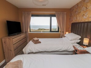 A hotel room with a bed, a TV, a window with curtains, and a view of the sea. - Bay View (Filey)