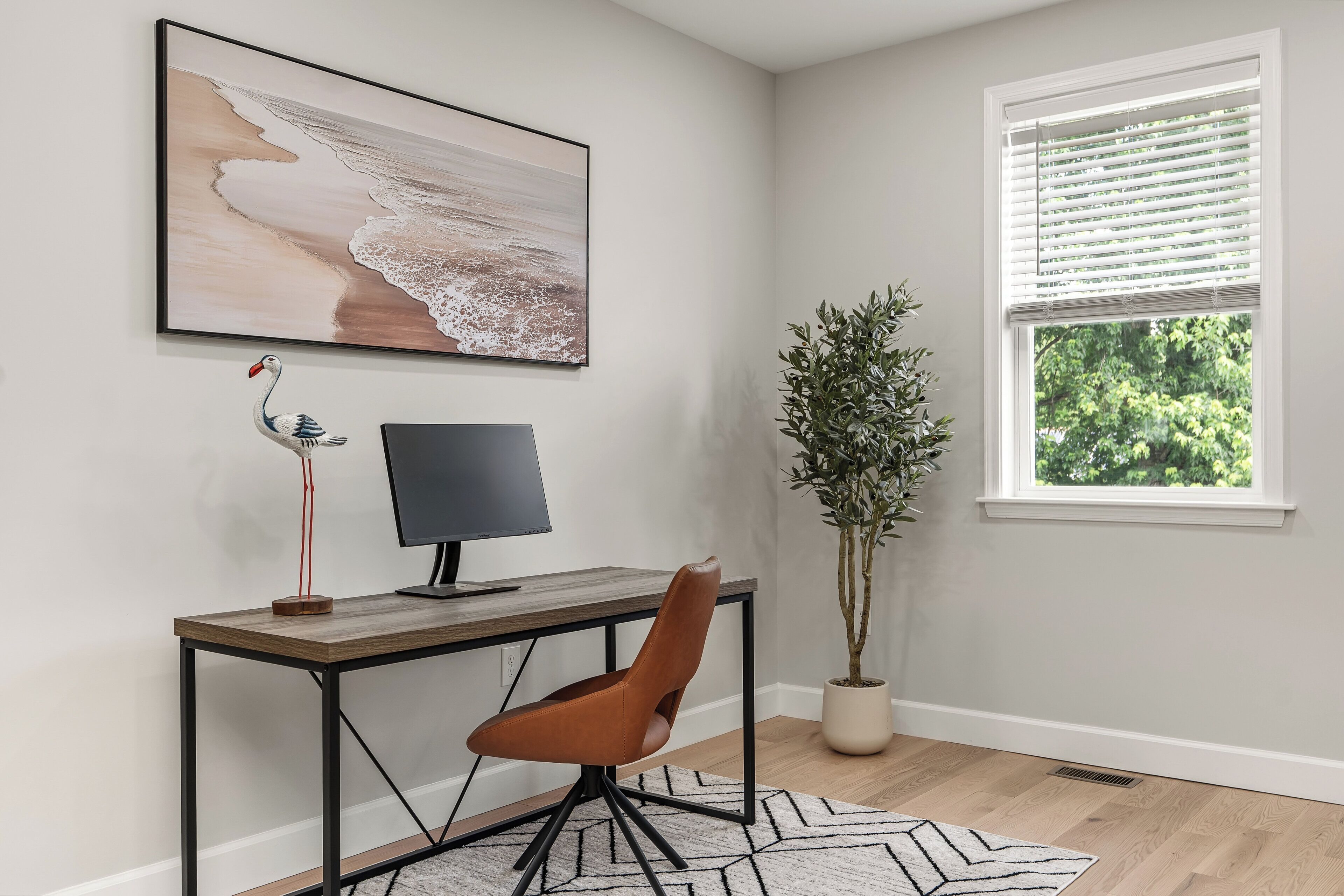 Un espace de bureau moderne comprenant un bureau, une chaise, un ordinateur, une œuvre d’art et une fenêtre avec des stores.