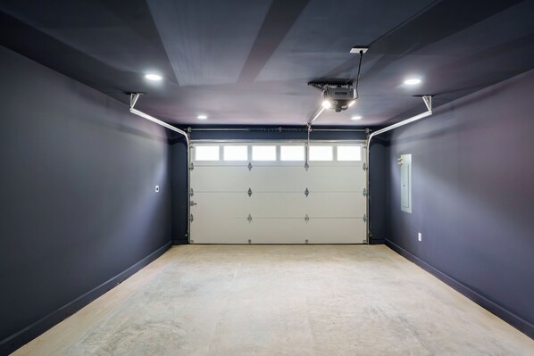 A garage with a large door, overhead lighting, and a concrete floor. - Stay Blue Heron, Coastal Comfort in Charlestown (Charlestown)