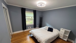 Una camera da letto con un letto, un comodino, una finestra con tende e una ventola a soffitto.