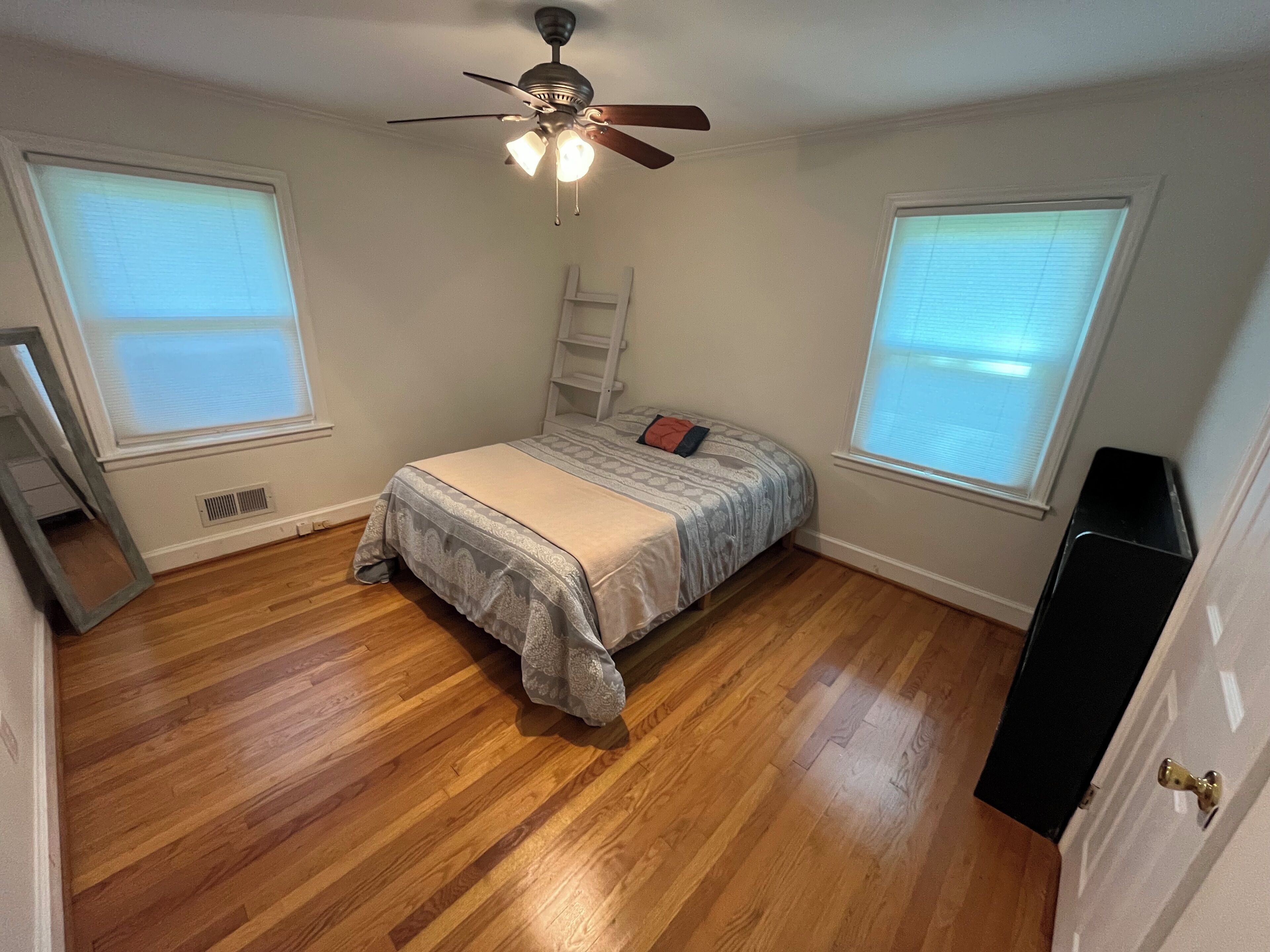 A bedroom with a bed, a ceiling fan, and two windows.