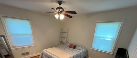 A bedroom with a bed, a ceiling fan, and two windows.